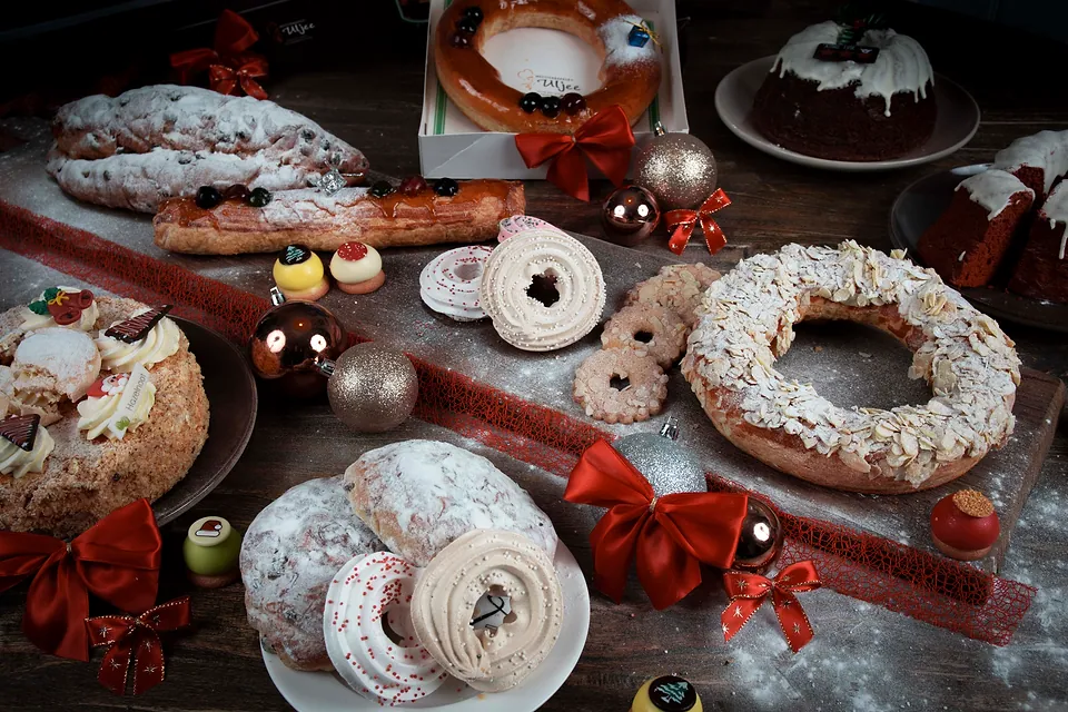 Kerststol, amandelkransen en taartjes op een donkere houten tafel met rode strikken
